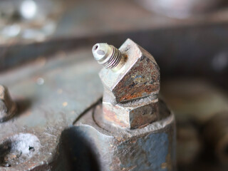 Close-up of a heavily worn and rusted metallic hydraulic fitting or elbow with a threaded connection, attached to a dark industrial machine component