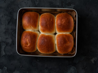 Homemade buns in a baking dish on a dark background, top view