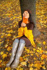 Portrait of full length Brunette girl sits on autumn leaves texture background at fall forest in park Young adult Asian woman in long leather high boots. 