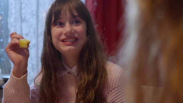 Girl smiling and talking with relatives at festive family dinner enjoying Christmas turkey celebrating the holiday season at home with Christmas tree, glowing lights, warm atmosphere of togetherness