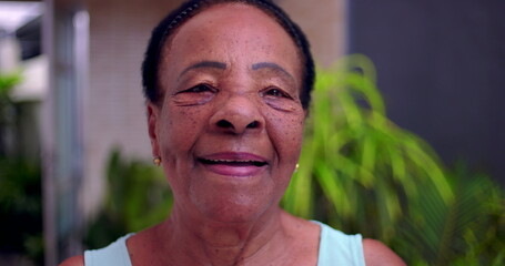 Close-up of elderly African American woman smiling warmly, vibrant expression of joy and positivity, outdoor setting with greenery, concept of active and happy senior lifestyle