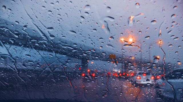 Atmospheric view of a rainy highway at dusk with water on the windshield and blurred taillights