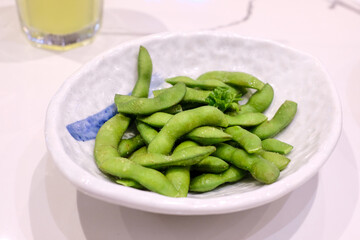 Fresh green edamame served in a ceramic bowl on a white table, representing healthy Asian food and vegetarian cuisine. Perfect for restaurant menus, healthy lifestyle blogs, or wellness