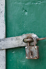 Old rusty padlock securing green wooden door