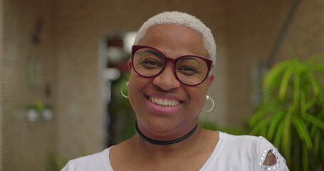 Close-up portrait of African American woman smiling warmly, wearing glasses, vibrant expression of...