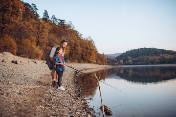Dad and daughter fishing in autumn nature, standing on lake shore.