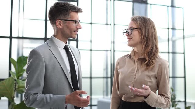 A man and a woman are talking in a room with a window