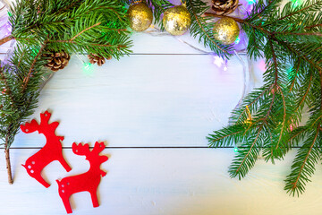 Spruce branches with cones, golden balls and red decorative deer beautifully frame the wooden background