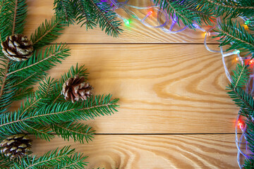 Green spruce branches with golden balls, cones and garland decorate the wooden background