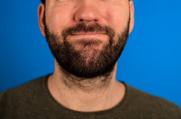 Obraz premium A close-up shot of a man's face with a dark beard, smiling, and a blue backdrop. The image highlights the man's facial features and beard in a s