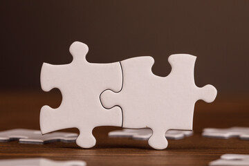 Image of two white puzzle pieces joined together on a wooden surface, symbolizing teamwork, problem-solving, and finding solutions. Great for bu