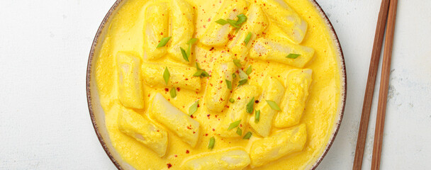 Delicious korean tteokbokki rice cakes served in a creamy cheese sauce, topped with green onion slices, presented in a bowl with chopsticks, authentic food of Korea