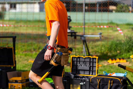 Trade apprentice walking past tool boxes wearing toolbelt holster