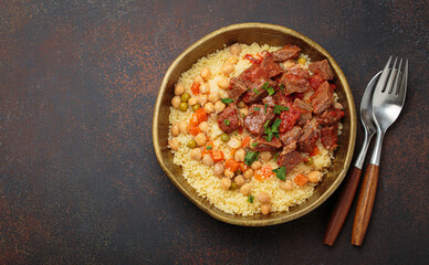 Traditional dish of Maghreb cuisine, a Moroccan couscous with lamb or beef, vegetables, chickpeas, and peas in a rustic bowl with cutlery on dark background, copy space