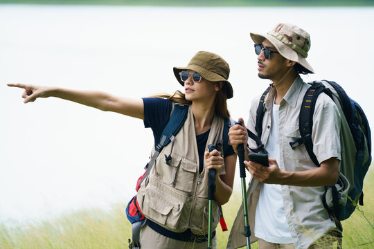 Asian hikers checking map on smartphone during outdoor adventure.