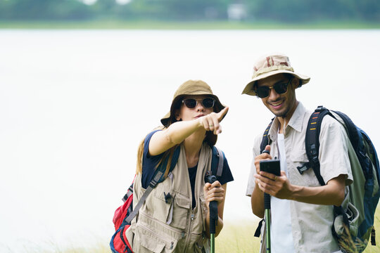 Asian hikers checking map on smartphone during outdoor adventure.
