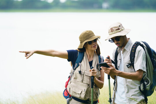 Asian hikers checking map on smartphone during outdoor adventure. - Powered by Adobe