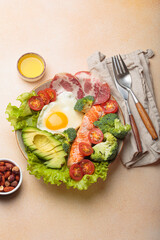 Healthy ketogenic diet concept showing a balanced meal on plate with salmon, avocado, fried egg, bacon, broccoli, tomato, and fresh salad, promoting low carb and high fat eating