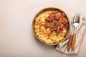 Traditional dish of Maghreb cuisine, a Moroccan couscous with lamb or beef, vegetables, chickpeas, and peas in a rustic bowl with cutlery on beige background, copy space
