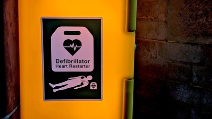 Automated External Defibrillator (AED) sign on a brightly illuminated yellow wall cabinet