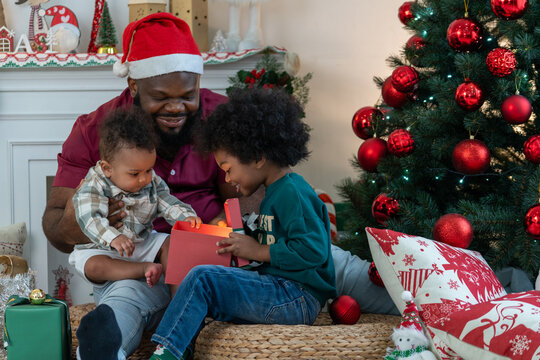 Happy African American dad with two son children celebrating Christmas. Black father and kids opening Christmas gifts. - Powered by Adobe