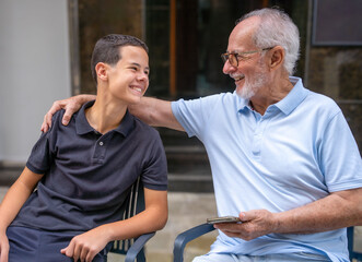 Grandfather and grandson looking each other having a great conversation sitting on a terrace outdoors.