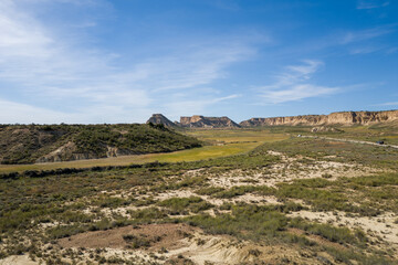 This landscape photo was taken in Europe, Spain, Navarre, in summer. It shows the green fields and cliffs in the Bardenas Reales, under the Sun.