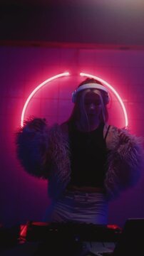 Woman DJ dancing in night neon party. Female disk jockey playing electronic music on techno rave, wear fur coat. Young girl jumping on set or stage, club mixer controller. Artist make modern sound