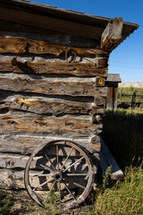 An old wagon wheel leaning against a vintage homestead cabin in the Western U.S.