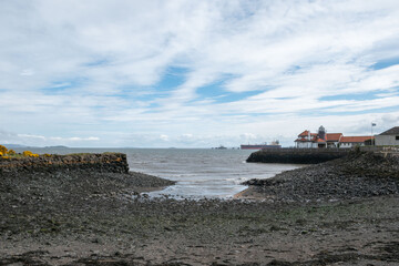 Scenic coastal view featuring a rocky shoreline and distant ships under a blue sky.