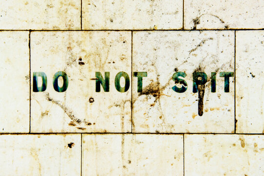 Do not spit sign painted on dirty tiled wall.