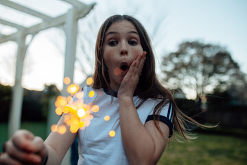 Young preteen girl holding a sparkler in the garden