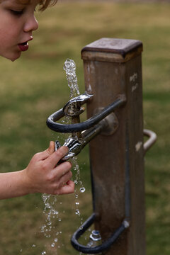 child drinking from a public water fountain