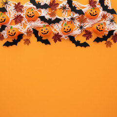 Composizione di decorazioni di Halloween con ragnatela, mini zucche intagliate, pipistrelli neri e ragni su sfondo arancione brillante.