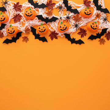 Composizione di decorazioni di Halloween con ragnatela, mini zucche intagliate, pipistrelli neri e ragni su sfondo arancione brillante.