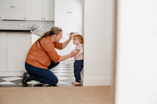 Mother measuring toddler daughters height against the wall