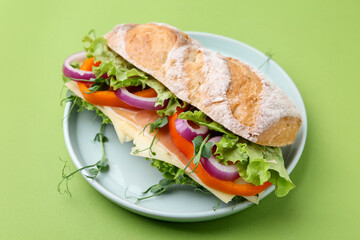 Delicious ciabatta sandwich with prosciutto, cheese and vegetables on green background, closeup