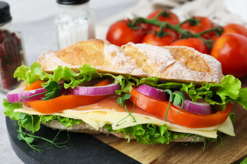Delicious ciabatta sandwich with prosciutto, cheese and vegetables on board, closeup