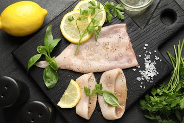 Pieces of raw squid, lemon and herbs on black table, flat lay