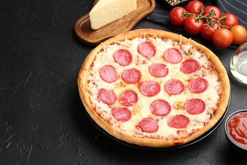 Delicious pepperoni pizza and ingredients on black table, closeup