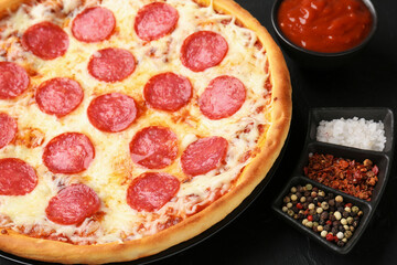 Delicious pepperoni pizza and ingredients on black table, closeup