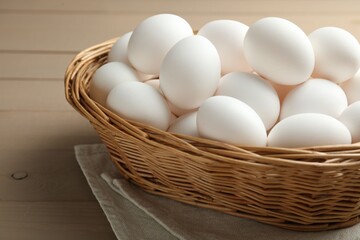 Many raw chicken eggs in wicker basket on wooden table, closeup