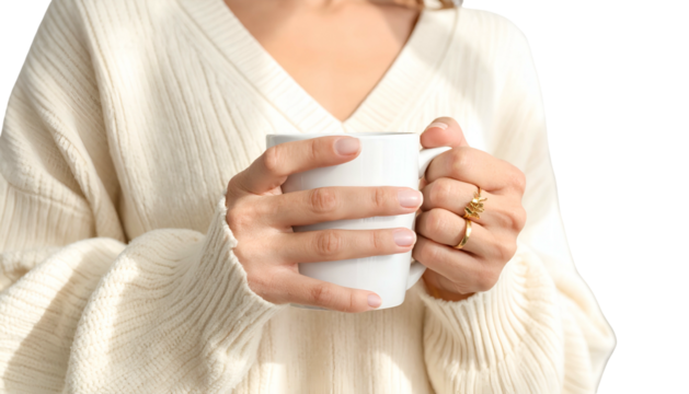 A person holds a white mug in both hands, wearing a sweater and rings