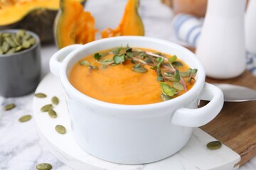 Delicious pumpkin soup with seeds and microgreens in bowl served on table, closeup