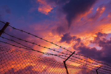 A fence with barbed wire and a beautiful sunset in the background