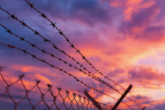 A fence with barbed wire on it and a beautiful sunset in the background