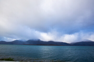 Autumn landscape of the Lyngen Alps in Northern Norway with snowy peaks, dramatic clouds, and a tranquil fjord.