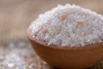 Closeup of coarse pink himalayan salt crystals in a small clay bowl on a burlap background