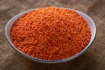 Bowl of vibrant red lentils on a rustic burlap background, showcasing their texture and color
