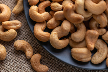 Closeup shot of roasted cashew nuts spilling from a dark plate onto a textured surface, showcasing their natural shape and color